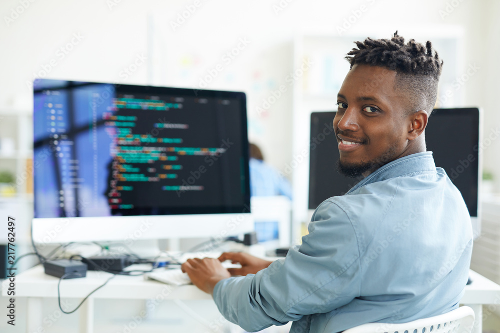 Sticker happy guy looking at you while sitting by workplace and working with software