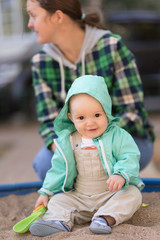 mother and child play in sandbox with green scoop
