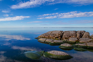 Fototapeta na wymiar Cracked stones. The stones go into the water. Horizon on the water. Wild nature. Coast line with stones. Karelia. Ladoga lake. Russia. The nature of Karelia.