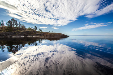The clouds are reflected in the lake. The stones go into the water. Horizon on the water. Wild nature. Islands on the Ladoga lake. Karelia. Ladoga lake. Russia. The nature of Karelia.