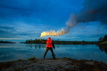 A man stands on an island with a torch in his hand. Smoke bomb. A signal for help. The man in the rescue jelly. At night, a man signals a smoke sword.