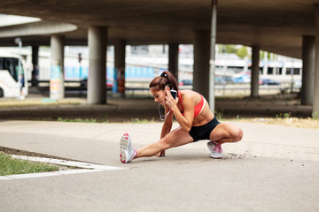 Female runner stretching and relaxing on city street after jogging.