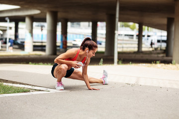 Naklejka premium Female runner stretching and relaxing on city street after jogging.