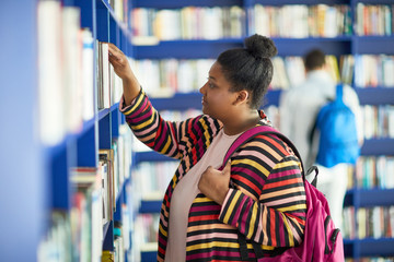 Serious concentrated fat African-American student girl in colorful stripped cardigan holding pink...