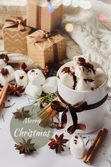 Obraz na płótnie Canvas Winter Christmas New Year hot drink. Cup of hot chocolate or cocoa with marshmallow, gift boxes with ribbon, fir branch, star anise, cinnamon on white knitted background