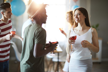Happy young intercultural couple with drinks having talk at home party while dancing
