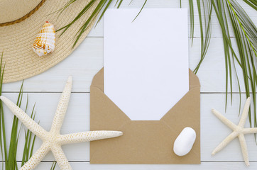 Mockup envelope with card template on white wooden background. Tropical palm leaf, summer hat,...