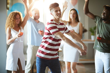 Fototapeta premium Young dynamic man dancing among his friends while enjoying home party