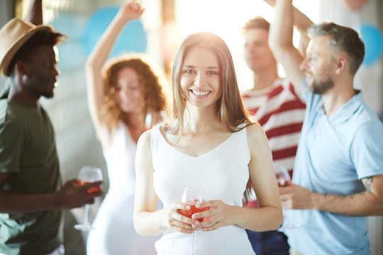 Charming woman with toothy smile looking at you among dancing friends at home party
