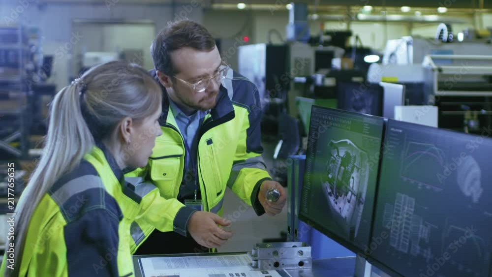 Poster At the Factory: Male Mechanical Engineer Holds Component while Female Chief Engineer Work on Personal Computer, They Discuss Details of the 3D Engine Model Design.