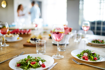 Homemade fruit drink, empty glasses, forks and plates with fresh salad on served table prepared for guests