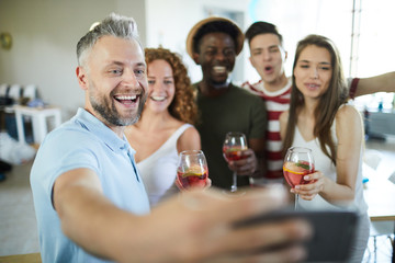 Happy man and his friends with drinks posing for selfie while enjoying home party