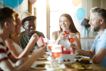 Group of joyful intercultural friends gathered by festive table to enjoy birthday party