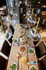 Appetizing meal served on wooden table in cozy cafe with lamps above and chairs around