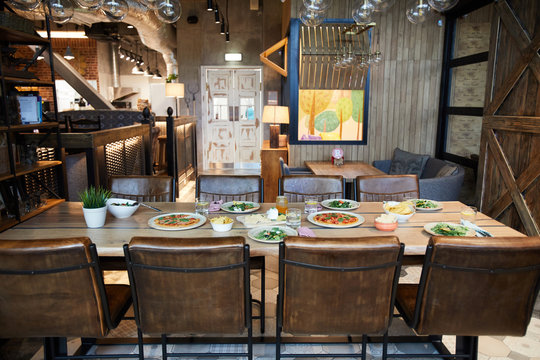 Wooden chairs around table served with food for several persons in cozy cafe