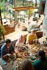 Group of young people gathered by wooden table served for dinner in cozy cafe