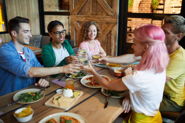 Happy young friends toasting with glasses of lemonade while enjoying dinner in cafe