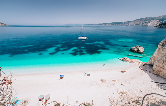 Fototapeta Azure water of Fteri beach, Cephalonia Kefalonia, Greece. White catamaran yacht in clear blue sea water. Tourists on sandy beach near azure lagoon