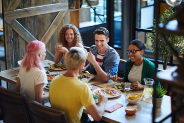 Happy guys and girls having talk by dinner while sitting by served table in cafe