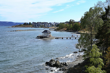 Lonely standing small cottage house in sea and footbridge connecting with coast in Oslofjord,  Norway. View to Oslo fjord in Fornebu district in Oslo, Norway.