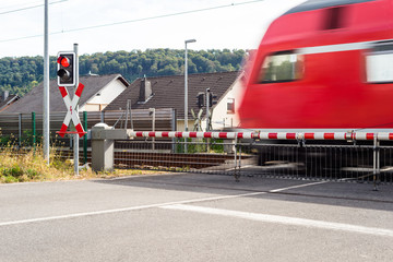 Naklejka premium A passenger train passing through a guarded railway crossing with closed barriers and a red light.