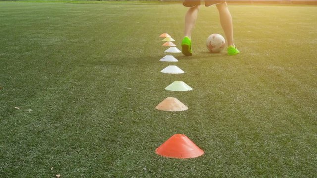 Soccer player running in football field leading ball between cones