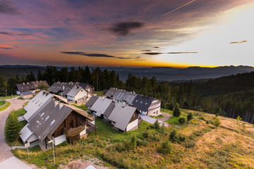 Resort mountain village houses surrounded foret at sunset.