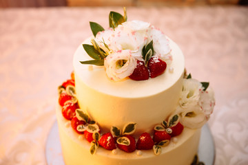 Close-up top view of a wedding three-story cream cake. Confectionery asteroids and dessert decorations for newlyweds, decorated with strawberries and white delicate flowers.