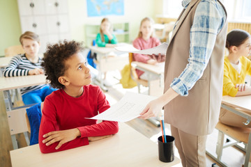 Teacher praising elementary student while getting school test back: content African-American boy...