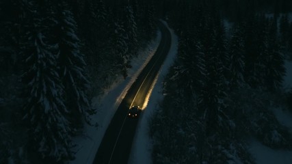 Aerial shot of cars driving through a snowy forest at night. - Powered by Adobe
