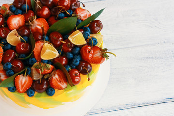 Biscuit bright yellow and white cake with fresh berries, green leaves, and lime on top of it