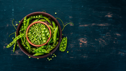 Green peas in a wooden plate. On a wooden background. Top view. Free space for your text.