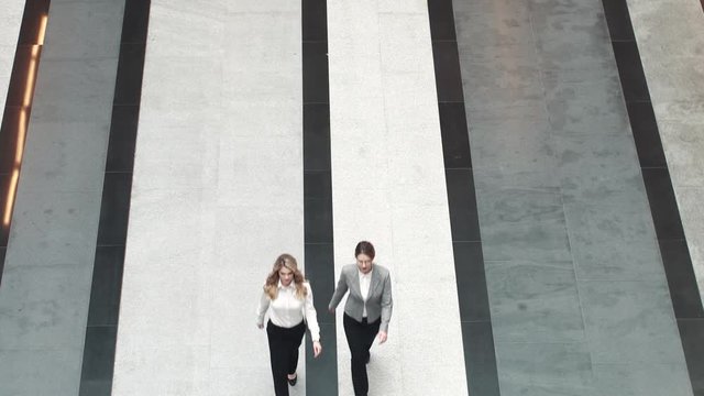 Head And Assistant In An Office Building. Two Business Women Walking Along The Corridor Of The Business Center. View From Above