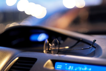 The glasses lie on the dashboard of the car. Night and light from the street lamps.
