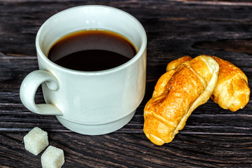 White cup with coffee and croissants on a wooden background, selective focus. The concept of breakfast.