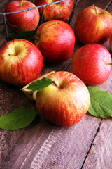 Ripe red apples with leaves on wooden background