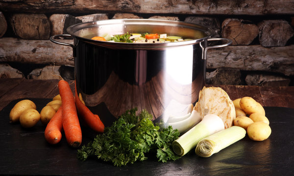 Broth with carrots, onions various fresh vegetables in a pot - colorful fresh clear spring soup. Rural kitchen scenery vegetarian bouillon or stock