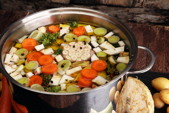 Broth with carrots, onions various fresh vegetables in a pot - colorful fresh clear spring soup. Rural kitchen scenery vegetarian bouillon or stock