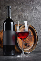 Red wine bottle with glass for tasting and wooden barrel in dark cellar