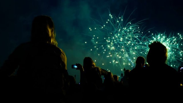 Crowd of people looks at the fireworks at night. Multicolored pyrotechnic show on the holiday.