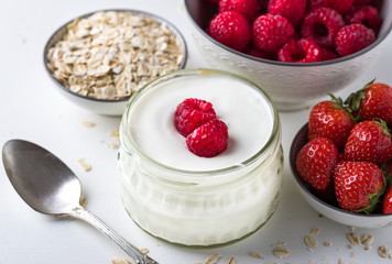 White yogurt in glass bowl with spoon and starwberries on white background.
