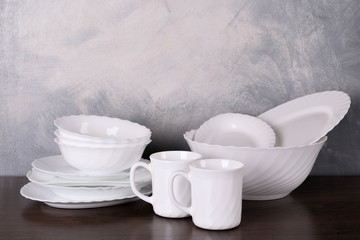 White dishware stacked on a wooden table against grey background on wooden table