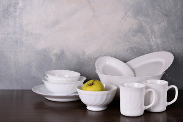 A set of wooden spoons in a white bowl on a gray background on a wooden table White dishware stacked on a wooden table against grey background on wooden table
