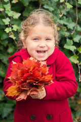 Laughing child holds a bouquet of autumn leaves.
