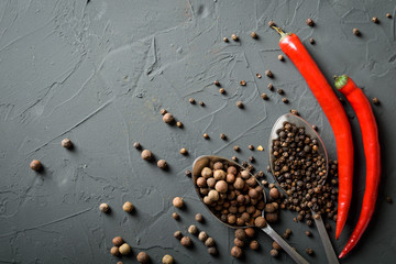  pepper black peas in metal antique spoons and hot chili peppers on a dark concrete beton background