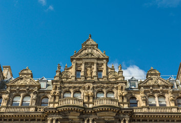 Naklejka premium Edinburgh, Scotland, UK - June 13, 2012: Top of monumental brown stone facade of Department store on corner of Princess and South David streets under blue sky.