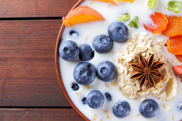 Oatmeal porridge with milk, fruits and peanuts on wooden background, healthy porridge with banana and peach slices, anise, dried apricots in milk