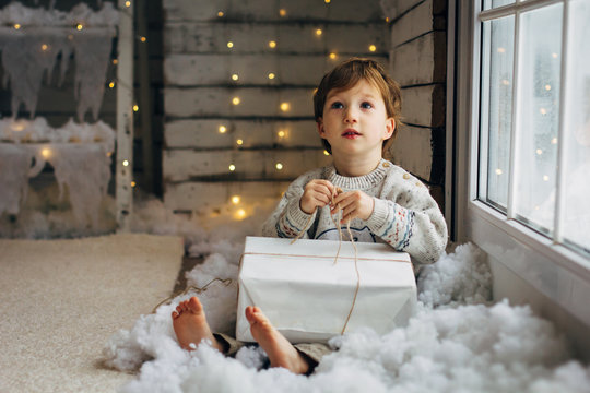 Beaming curlyhair boy opening his christmas gift. New Year lights background