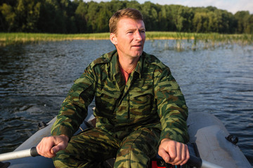 Naklejka premium Man fisherman in camouflage on a rubber boat floating in the lake.