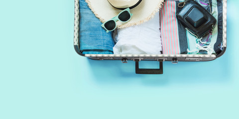 Open suitcase with female clothes for trip on pastel blue. Top view with copy space. Summer concept travel.